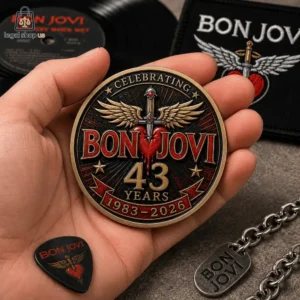 A commemorative Bon Jovi 43rd anniversary metallic coin held in a hand surrounded by music merchandise.