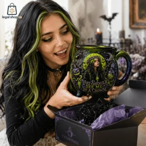 A woman with green-streaked black hair holding a themed cauldron mug with gothic art and text.